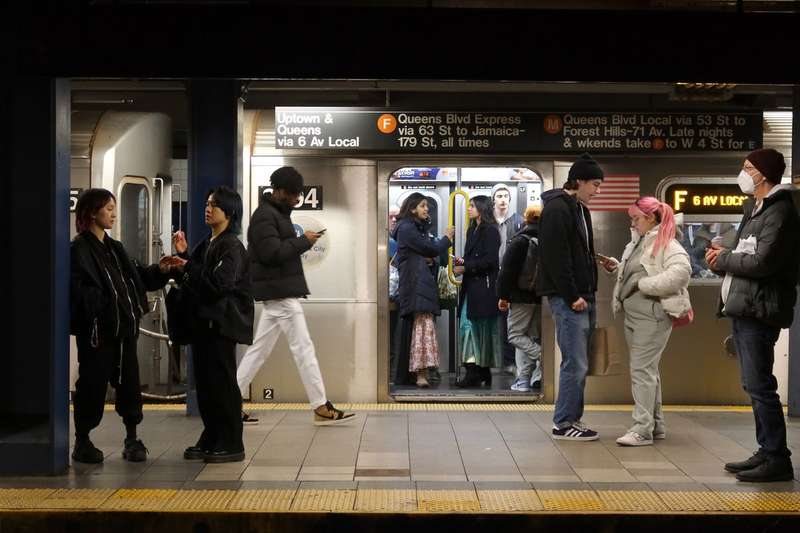 In an underground subway station, riders are seen inside an open subway train, and others are seen on the platform in the foreground waiting for their train.