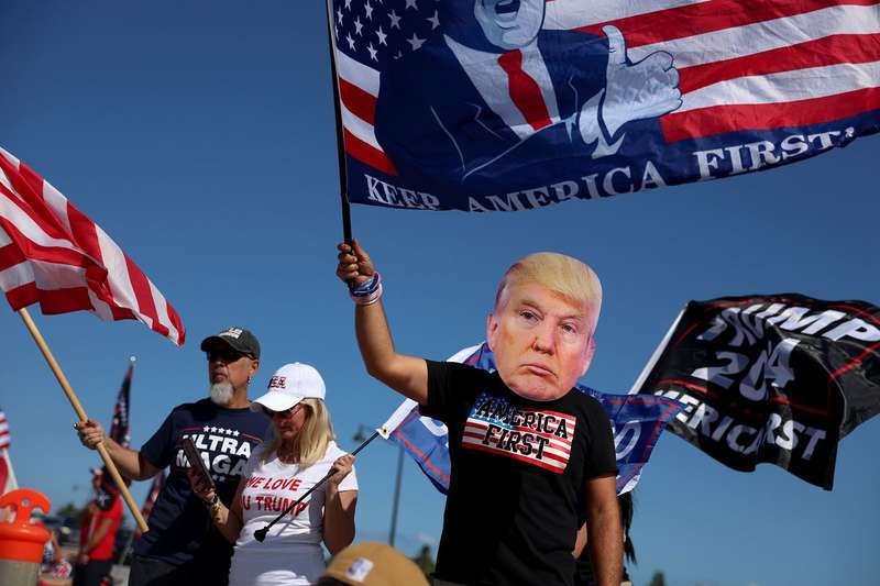 A person in a Trump mask waves an “America first” flag.