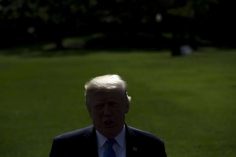 Trump seen from the shoulders up, in shadow, with the South Lawn in the background. 