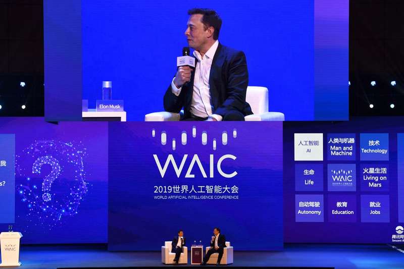 Elon Musk sits onstage holding a microphone.