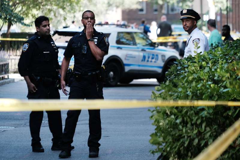 Police officers standing in front of police cars and behind caution tape.