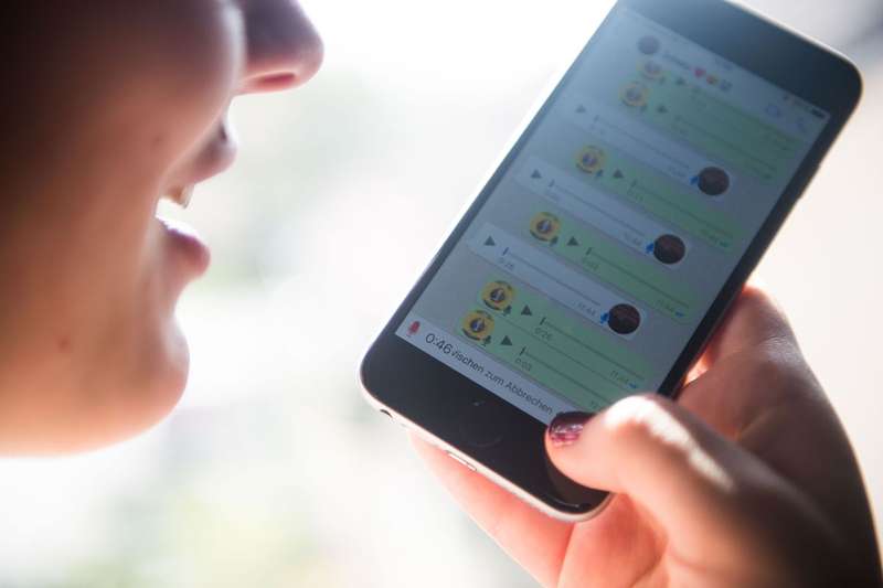 A person holds a phone in front of them and speaks into it. A messaging app is seen on the screen.